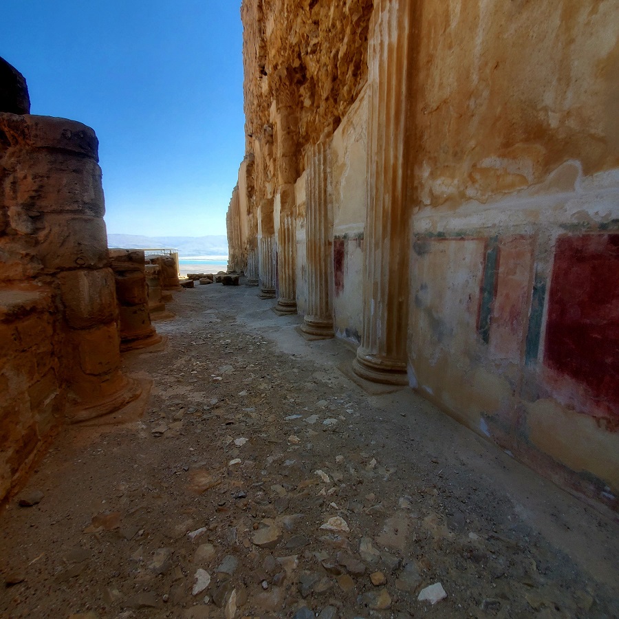 Columns of the palace. The plaster intact and the paintings of reds and greens still vibrant. The dead Sea can be seen in the background.