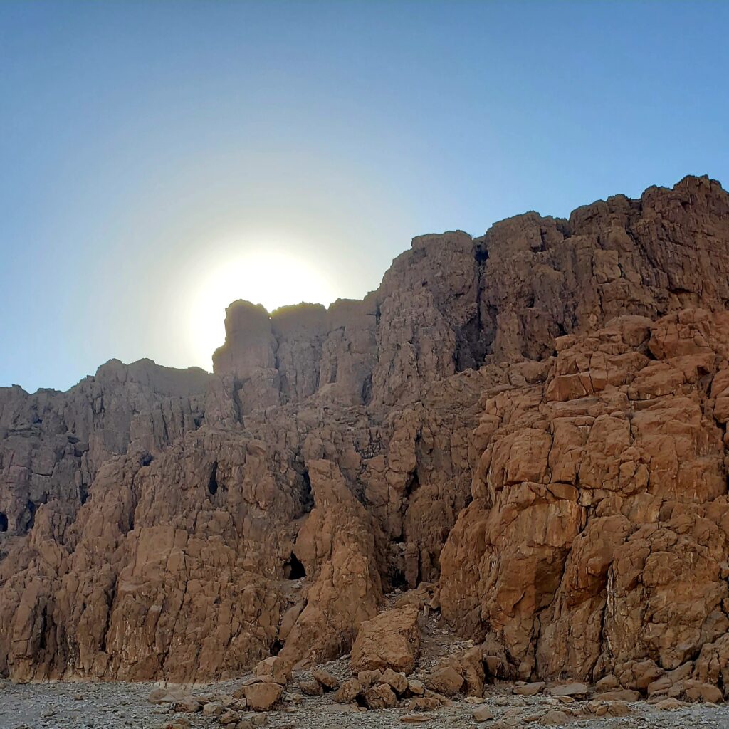 The Qumran caves. The black entrances to several in the mountainside. The setting sun cresting the mountaintop above.