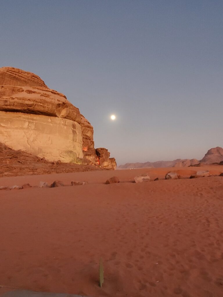 The moon over the sand and sandstone mountains, the lights of the camps on the stone. 