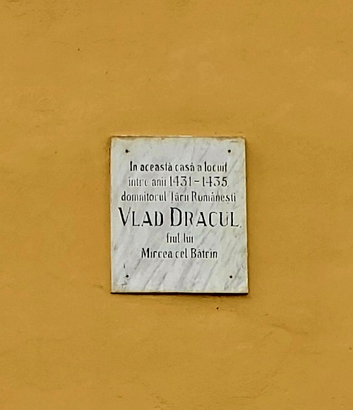 In the center of a bright yellow plastered wall is a white and grey marble plaque denoting the House of Dracul. Where Vlad Dracul was born.