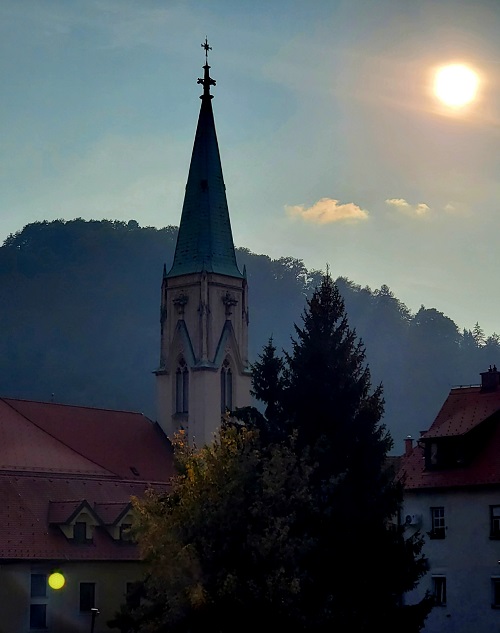 The church steeple in Celje outside the last minute hotel room. The sun is bright and sunset is not far away.